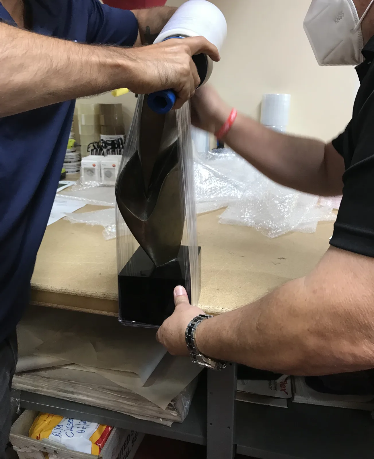 Packing team applying protective wrap to a fragile item